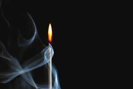 Burning match in smoke on dark background
