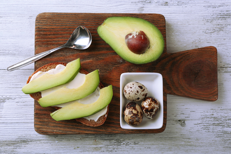 Slice of rye bread with sliced avocado and boiled quail eggson color wooden backgroundの写真素材