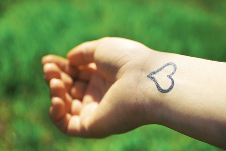Hand of young woman with heart tattooed in it, on green nature backgroundの写真素材