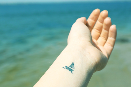 Close up of hand of young woman with ship tattooed in it, on sea backgroundの写真素材