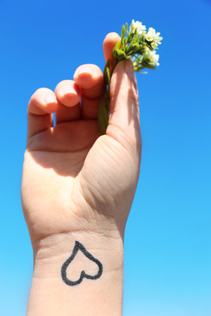 Hand of young woman with heart tattooed in it, on blue sky backgroundの写真素材