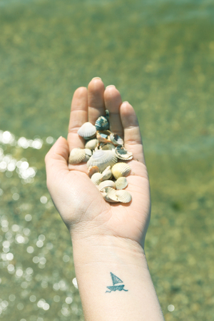 Close up of hand of young woman with ship tattooed in it, on sea backgroundの写真素材