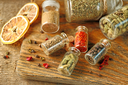Assortment of spices in glass bottles on cutting board, on wooden backgroundの写真素材
