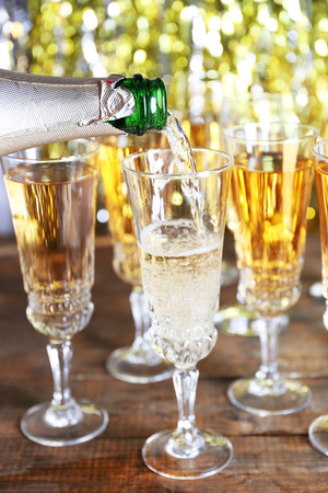 Pouring champagne from bottle into glasses on bright backgroundの写真素材