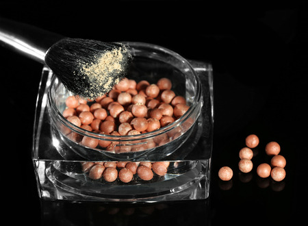 Jar with cosmetic powder balls and makeup brush, isolated on black