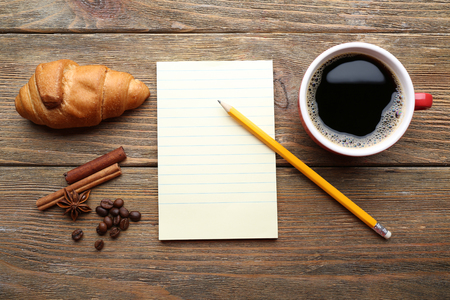 Cup of coffee with fresh croissant and blank sheet of paper on wooden table, top viewの写真素材