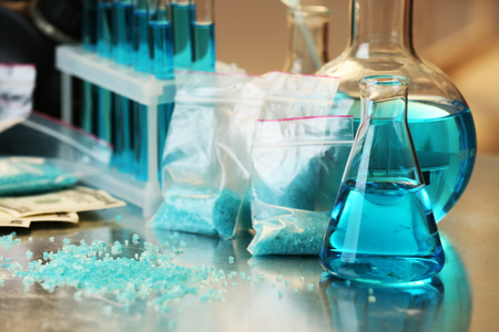 Blue methamphetamine and liquid in flasks on table in laboratoryの写真素材