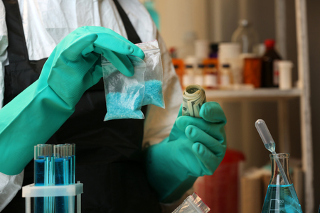 Chemists holding plastic bag with blue methamphetamine and money in laboratory