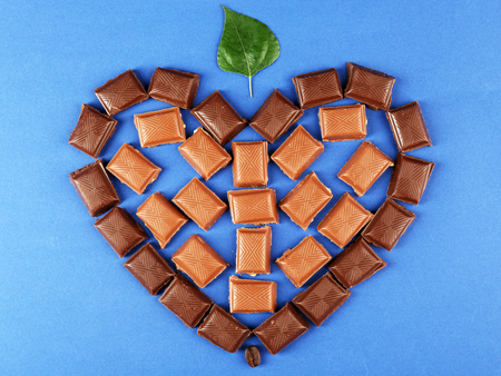 Chocolate pieces arranged in heart shape with green leaf on blue background