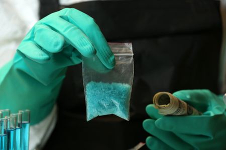 Chemists holding plastic bag with blue methamphetamine and money in laboratory