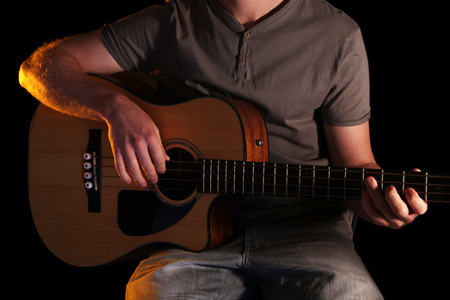 Young man playing on acoustic guitar on dark background