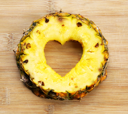 Pineapple slice with cut in shape of heart on wooden backgroundの写真素材