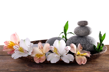 Spa stones with alstroemeria and bamboo in wooden tray with water isolated on whiteの写真素材