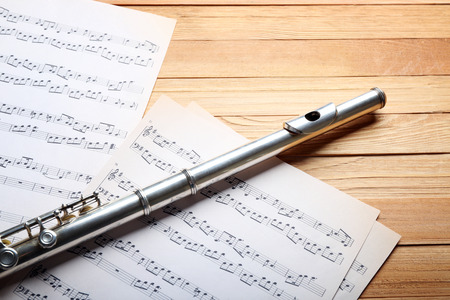 Silver flute with music notes on wooden table close upの写真素材