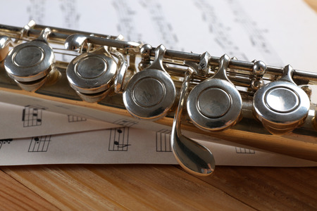Silver flute with music notes on wooden table close upの写真素材