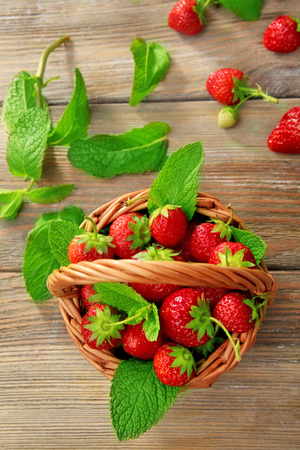 Ripe strawberries in wicker basket on wooden table, top viewの写真素材