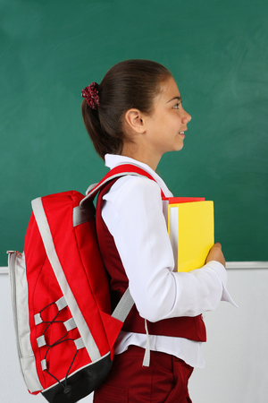 Beautiful little girl standing near blackboard in classroomの写真素材