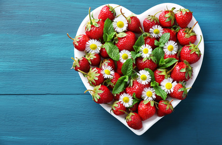 Red ripe strawberries on heart shaped plate, on color wooden backgroundの写真素材