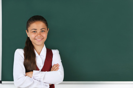 Beautiful little girl standing near blackboard in classroomの写真素材