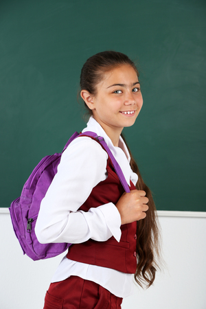 Beautiful little girl standing near blackboard in classroomの写真素材