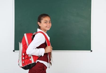 Beautiful little girl standing near blackboard in classroomの写真素材