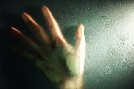 Female hand behind  wet glass, close-upの写真素材