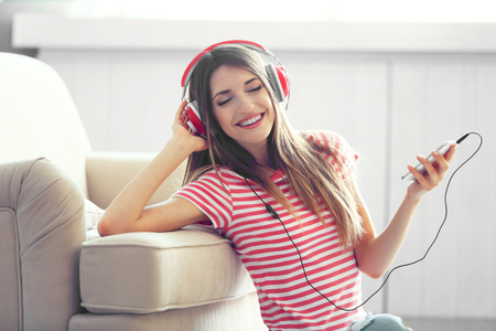 Woman listening music in headphones in roomの写真素材