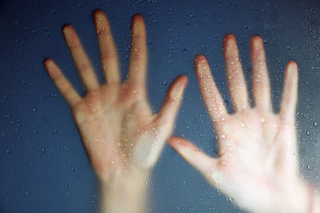 Female hand behind  wet glass, close-upの写真素材