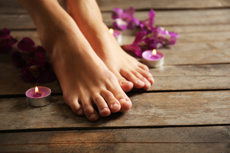 Female feet at spa pedicure procedure with flowers and candlelight on wooden backgroundの写真素材