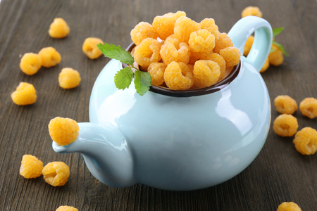 Yellow raspberries in teapot on wooden backgroundの写真素材