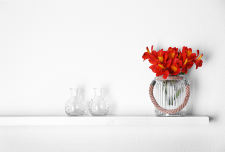 Decorative glass vases with flowers  on wooden shelf  on white wallpaper backgroundの写真素材