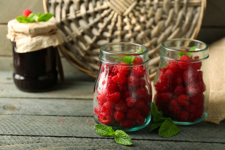 Sweet raspberries in glass jar on wooden  background