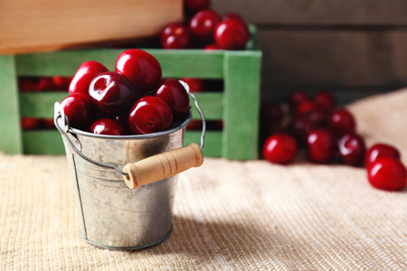 Sweet cherries with green leaves in bucket and wooden boxes, on wooden backgroundの写真素材