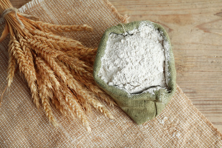 Whole flour in burlap bag with wheat ears on wooden table, closeupの写真素材