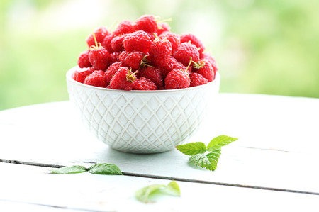 Fresh raspberries in bowl on wooden table on blurred nature backgroundの写真素材