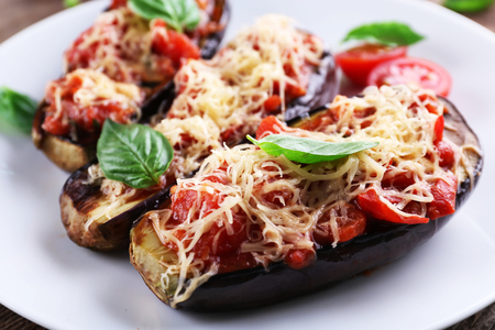 Dish of eggplant with cherry tomatoes and cheese in white plate on wooden table, closeupの写真素材