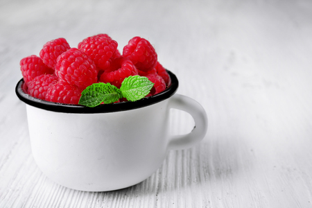 Fresh red raspberries in cup on wooden background