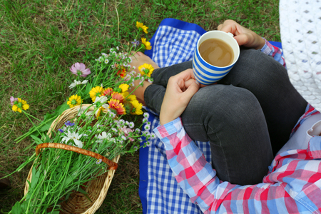 Young woman with cup of coffee sitting on meadow outdoorsの写真素材