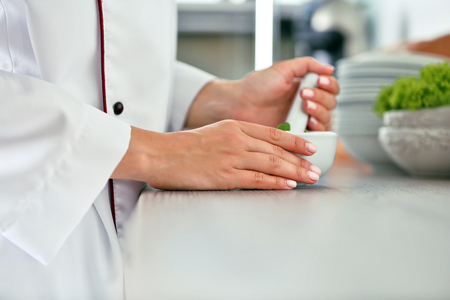 Cook hands with mortar with herbs on bright backgroundの写真素材