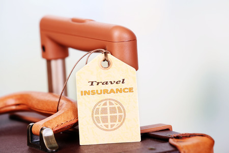 Suitcase with TRAVEL INSURANCE label on light blurred backgroundの写真素材