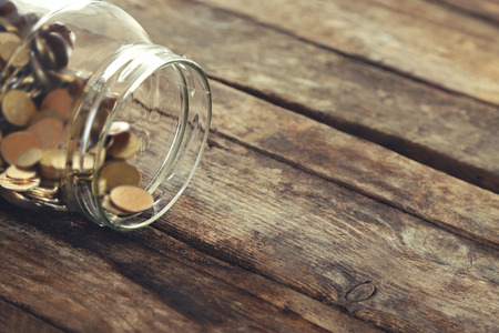 Coins in money jar on wooden background