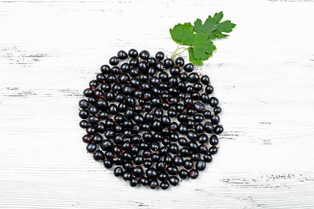 Heap of wild black currant with green leaves on wooden background