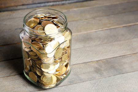 Glass jar with coins on wooden background