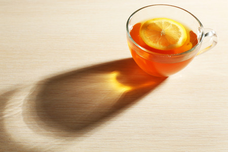 Glass cup of tea with piece of lemon on wooden table backgroundの写真素材