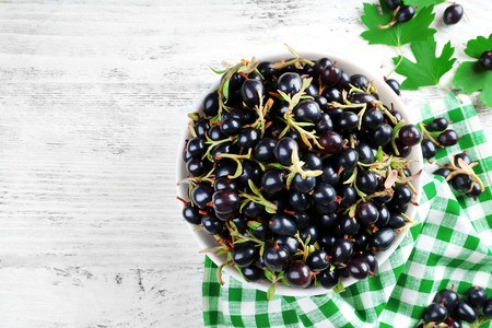 Ripe black currants in bowl on wooden table with checkered napkin, top viewの写真素材