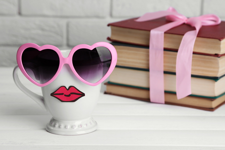 Vintage books and cup with lips on wooden table on brick wall backgroundの写真素材