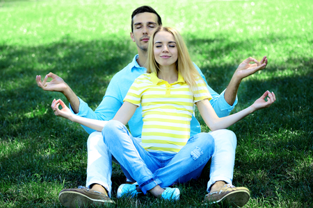 Young pregnant woman with husband sitting on green grass in parkの写真素材