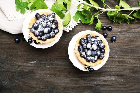 Delicious crispy tarts with black currants on white stand on wooden table, top viewの写真素材