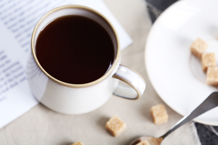 Cup of flavored coffee with lump sugar on table with napkin and newspaper, closeupの写真素材