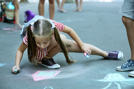 Cute small girl drawing with chalk on asphaltの写真素材